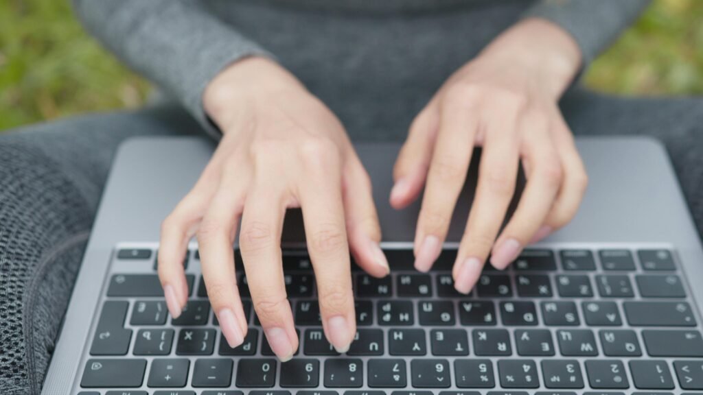 Hands typing on a laptop keyboard in an outdoor setting, capturing a modern, portable work environment.